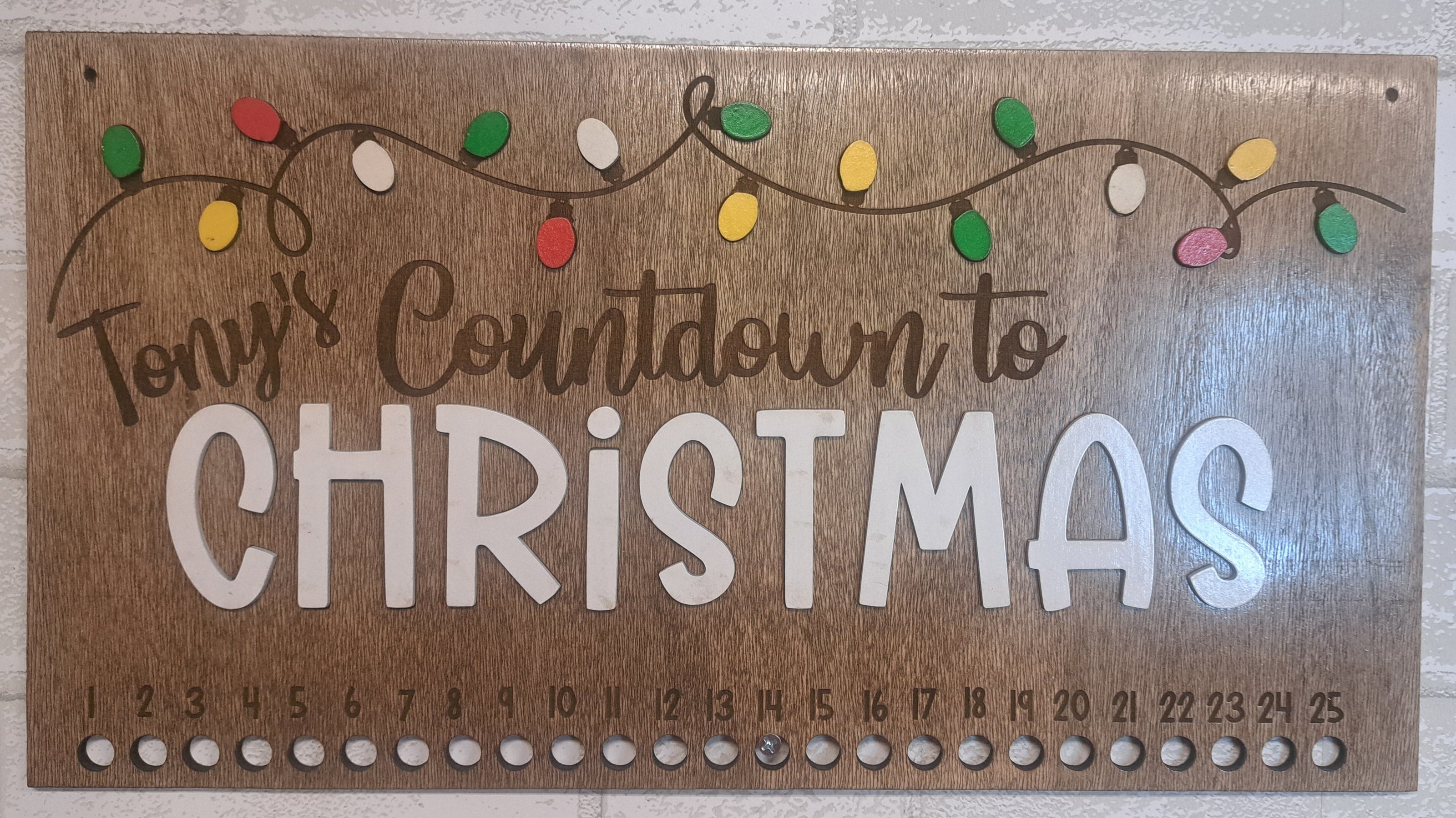 Wooden Christmas countdown sign with decorative lights on a light gray background