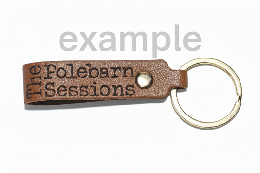 Brown leather keychain with 'The Pole Barn Sessions' engraving pictured on a white background